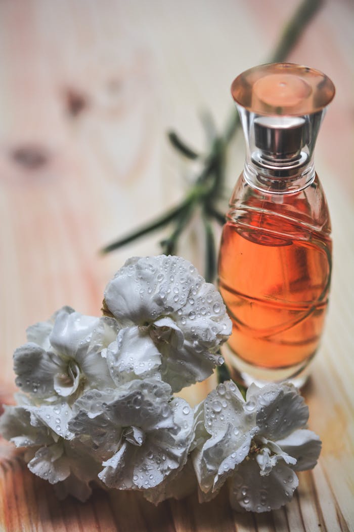 our-services-2 Glass perfume bottle alongside dew-kissed white carnation flowers on wood surface.